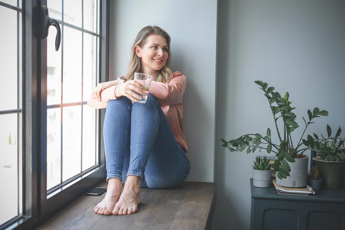 eine junge Frau mit einem Glas in der Hand sitzt auf einer Fensterbank